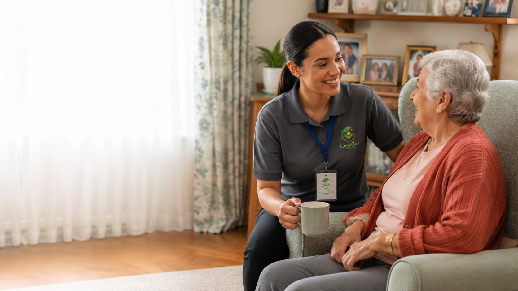 A support worker kneeling beside an older woman's armchair, sharing a cup of tea and a warm conversation